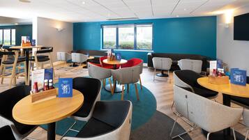 A modern dining area with round tables and chairs, a blue wall, and a window providing natural light.