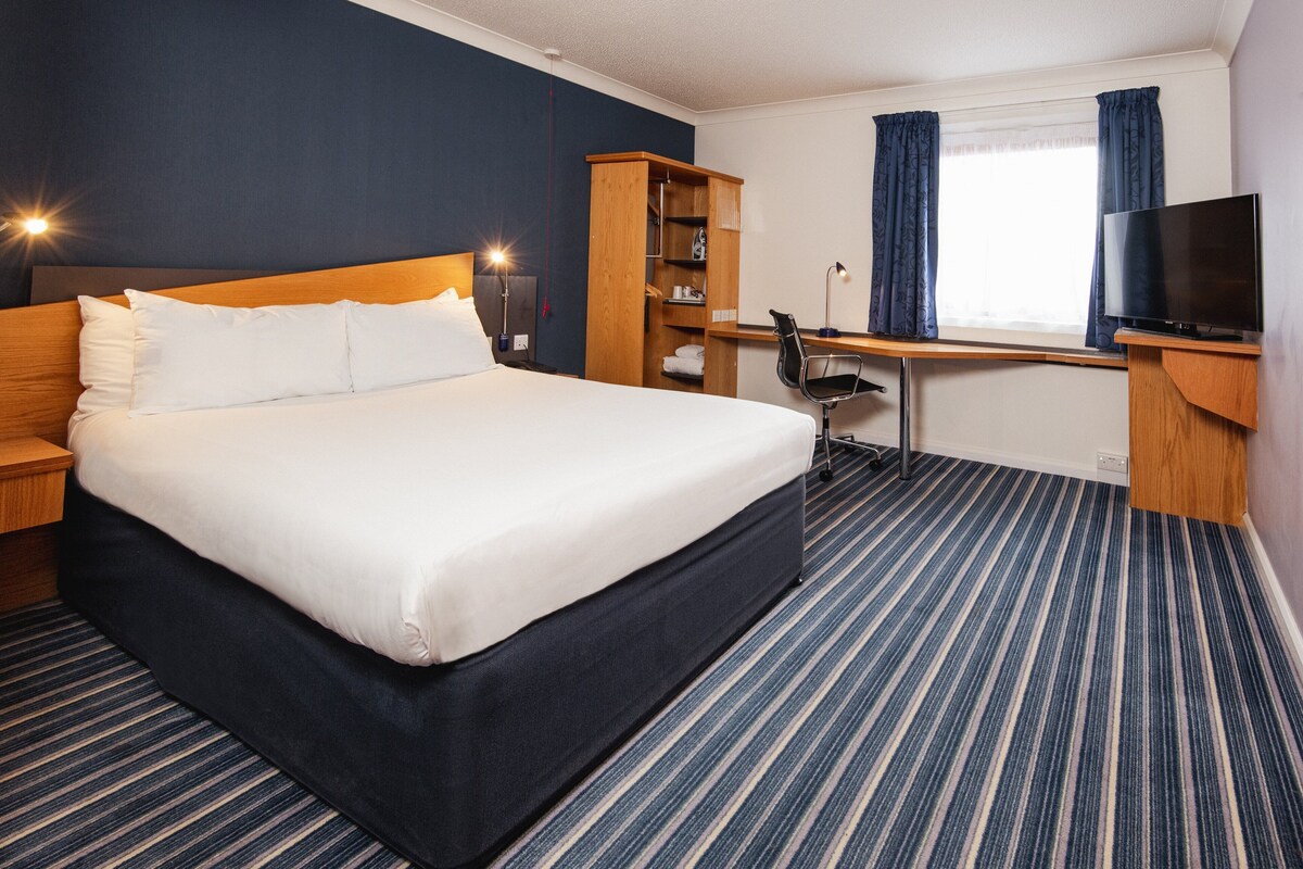Habitación de hotel con una cama grande, un escritorio con silla, un televisor y un armario.