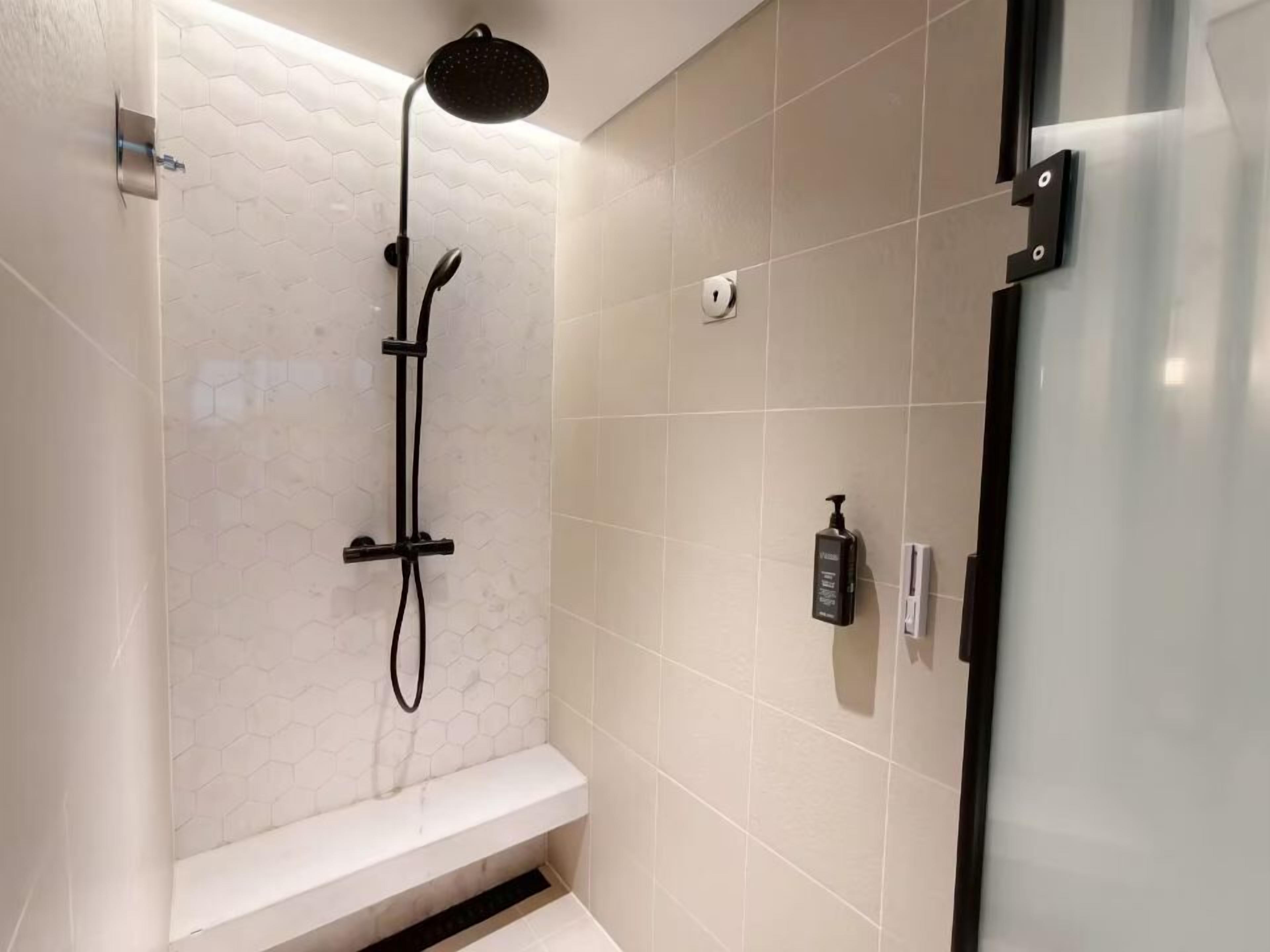 Eine Dusche mit Duschbrause, Sitzbank und Seifenspender an der Wand.