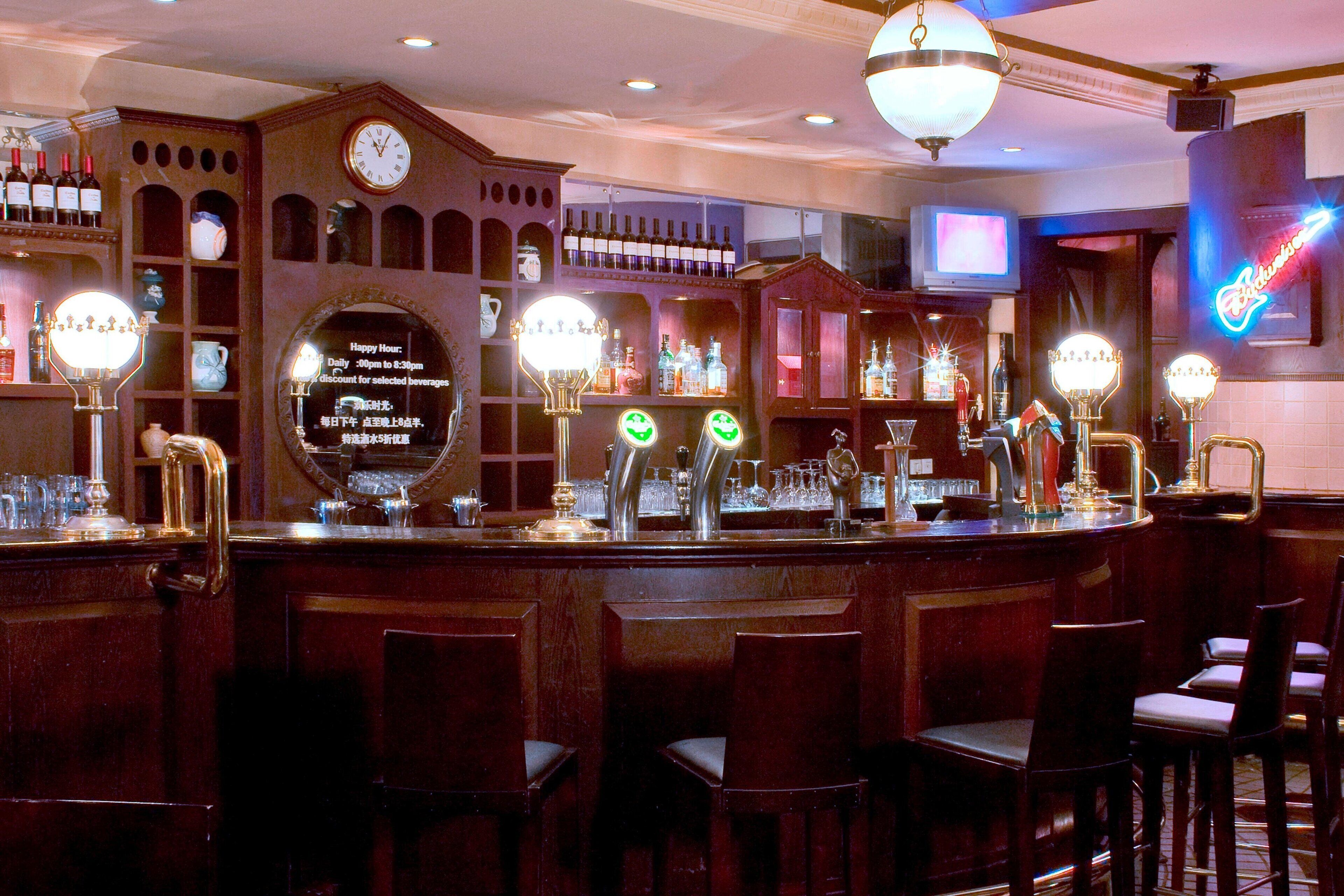 A bar area with a clock, shelves of bottles, and bar stools.