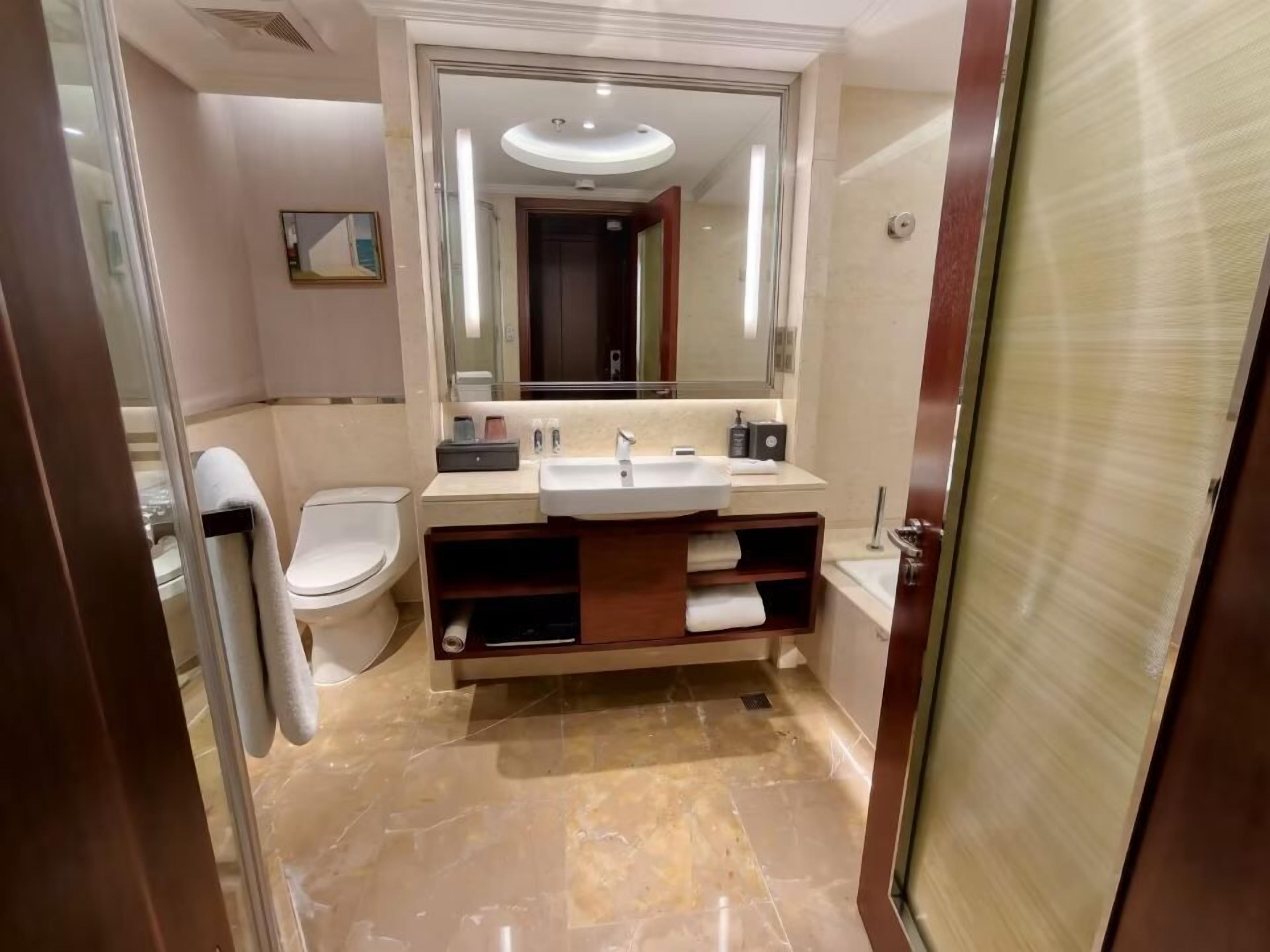 A modern bathroom with a marble floor, a large mirror, a toilet, and a sink with a vanity.
