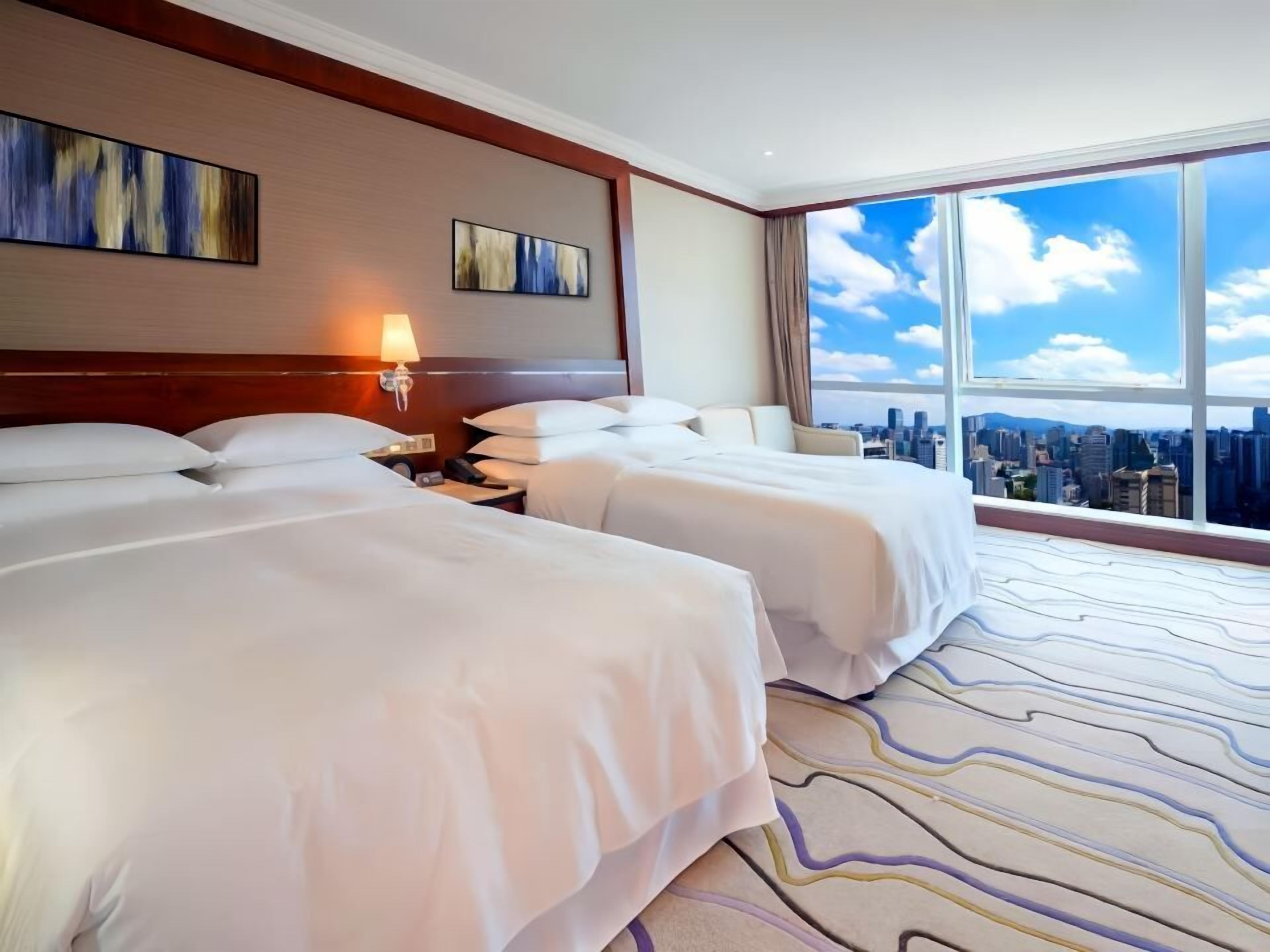 Ein Hotelzimmer mit zwei Betten, Blick auf die Stadt und Bildern an den Wänden.