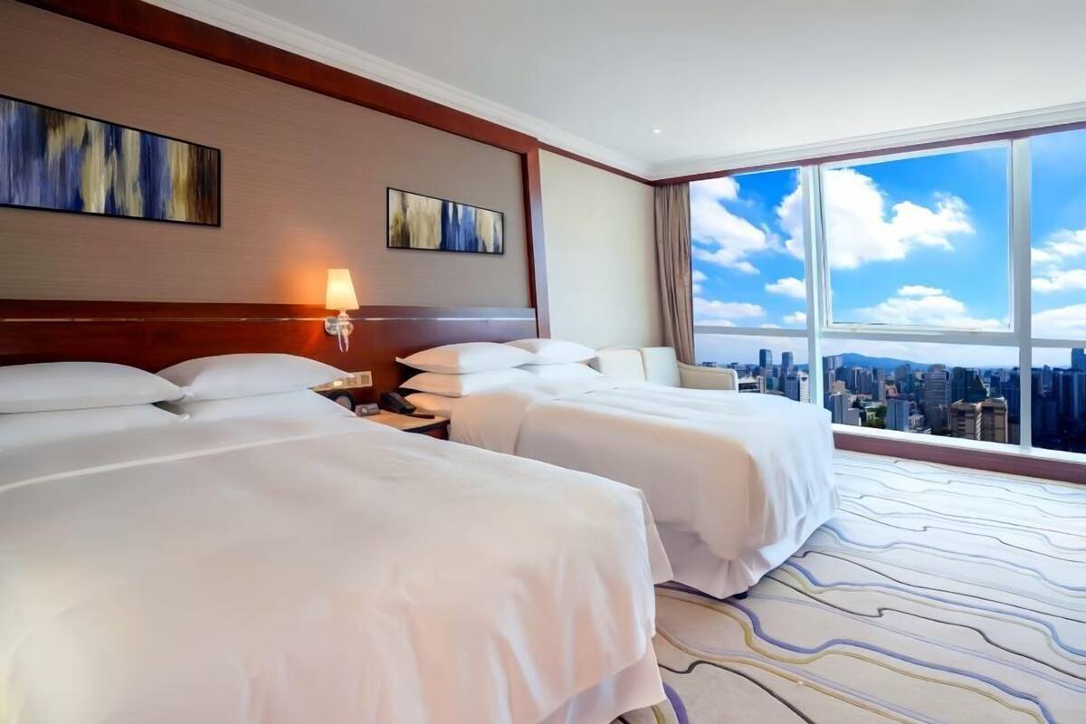 A hotel room with two beds, a city view, and artwork on the walls.
