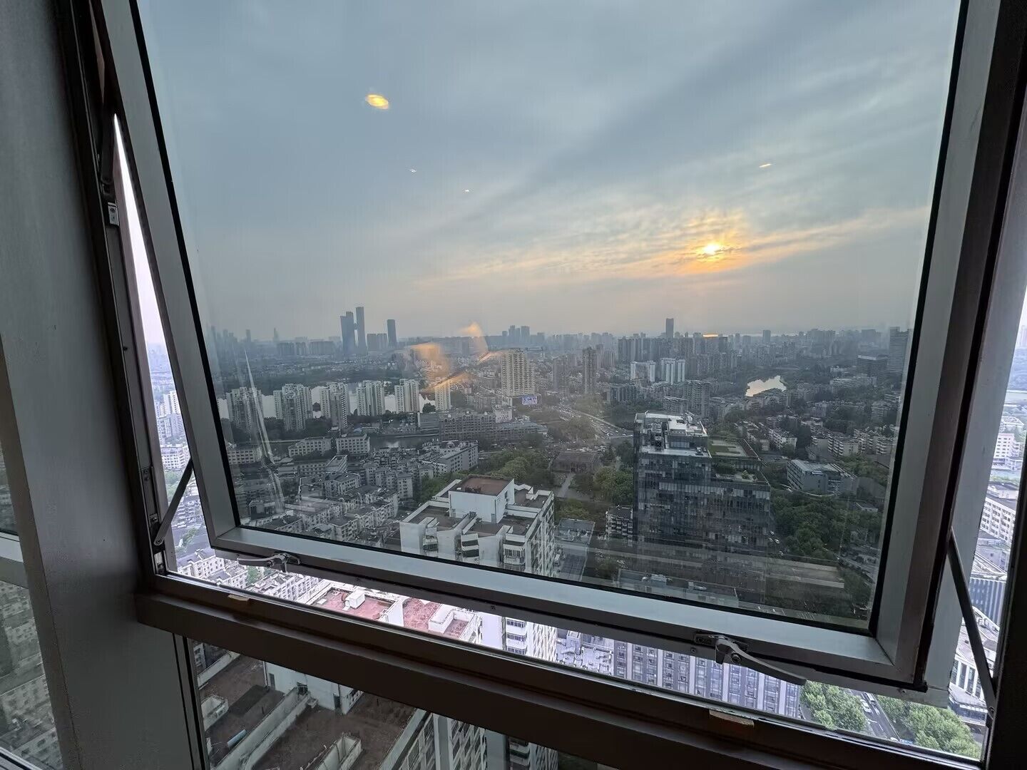 A cityscape view from a high-rise building with a clear sky and the sun setting in the distance.
