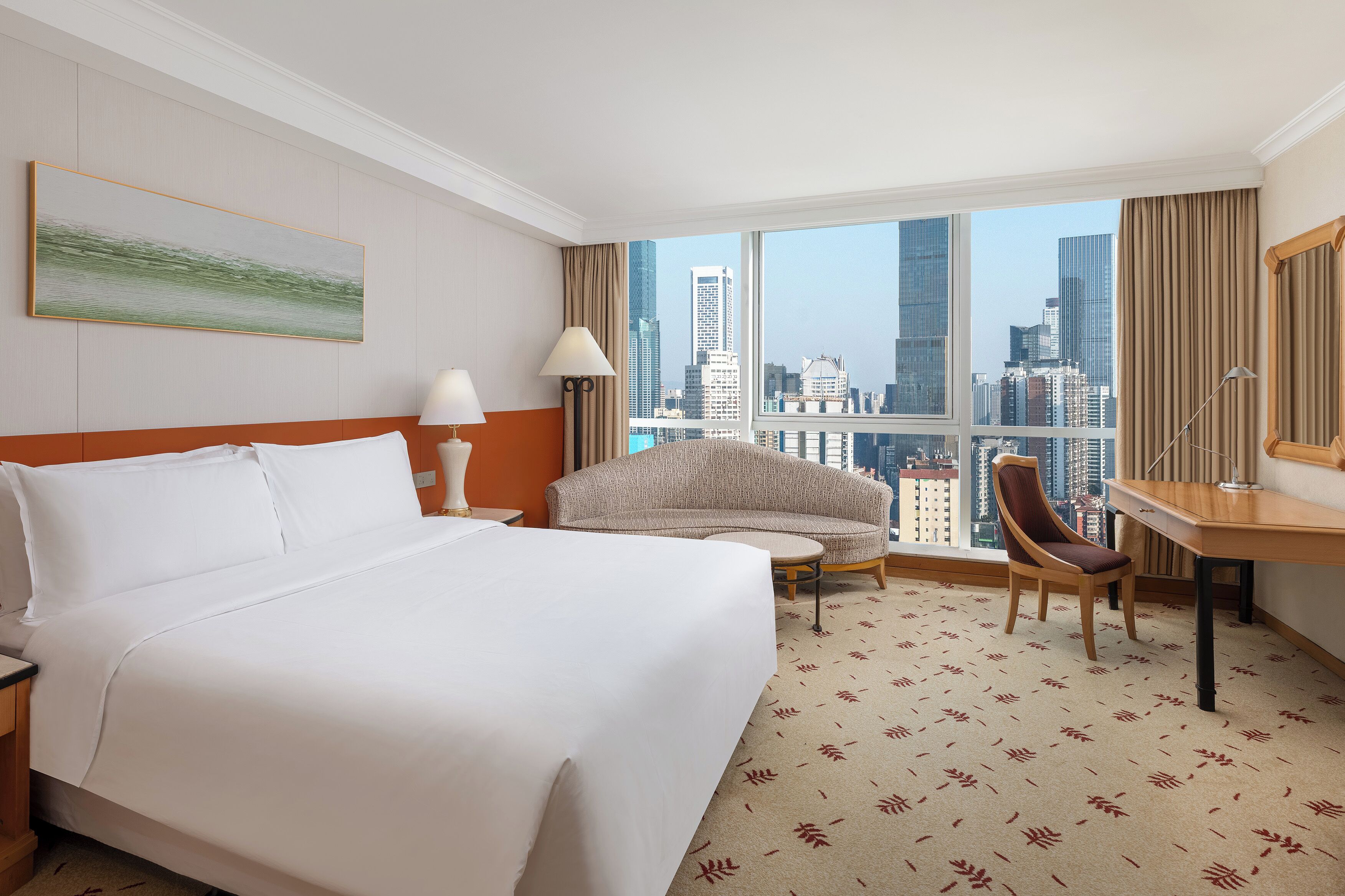 A hotel room with a large bed, a sofa, a desk, and a view of the cityscape.