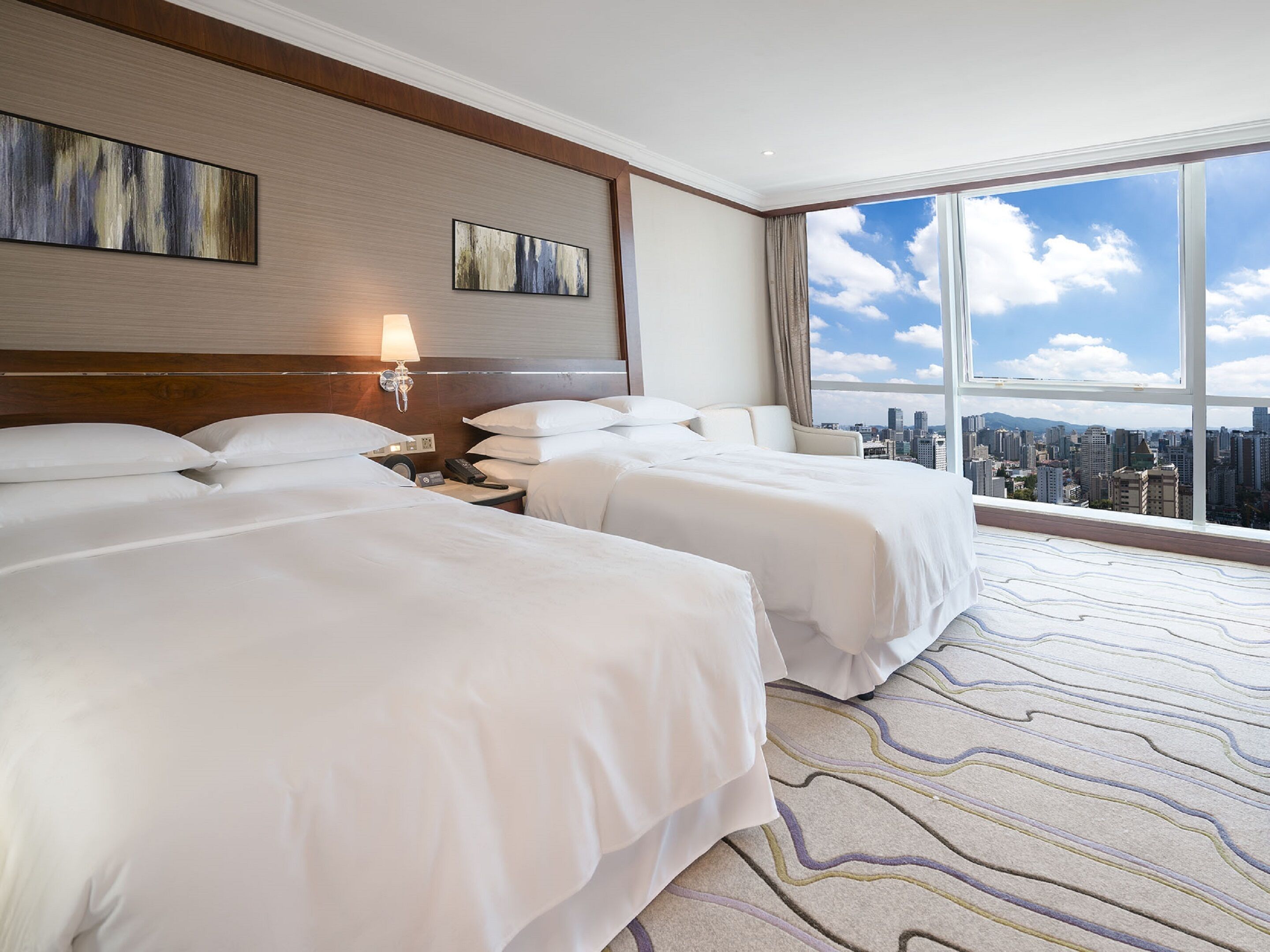 Habitación de hotel con dos camas, vista a la ciudad y un ventanal grande.