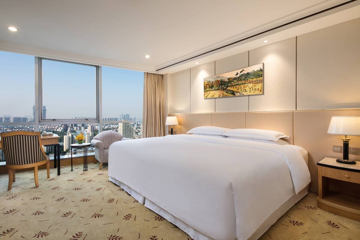 A hotel room with a large bed, a desk, a chair, and a view of the city.