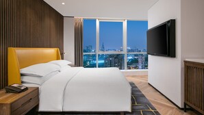 A modern hotel room with a large bed, a TV mounted on the wall, and a city view through large windows. - Sheraton Nanjing Kingsley Hotel (Nanjing)