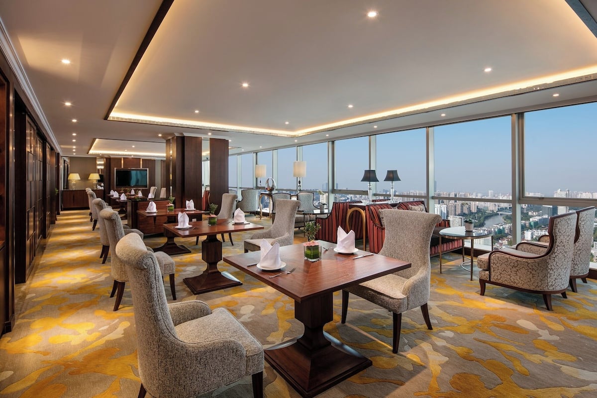 A modern hotel room with a large dining table, comfortable seating, a TV, and a city view.