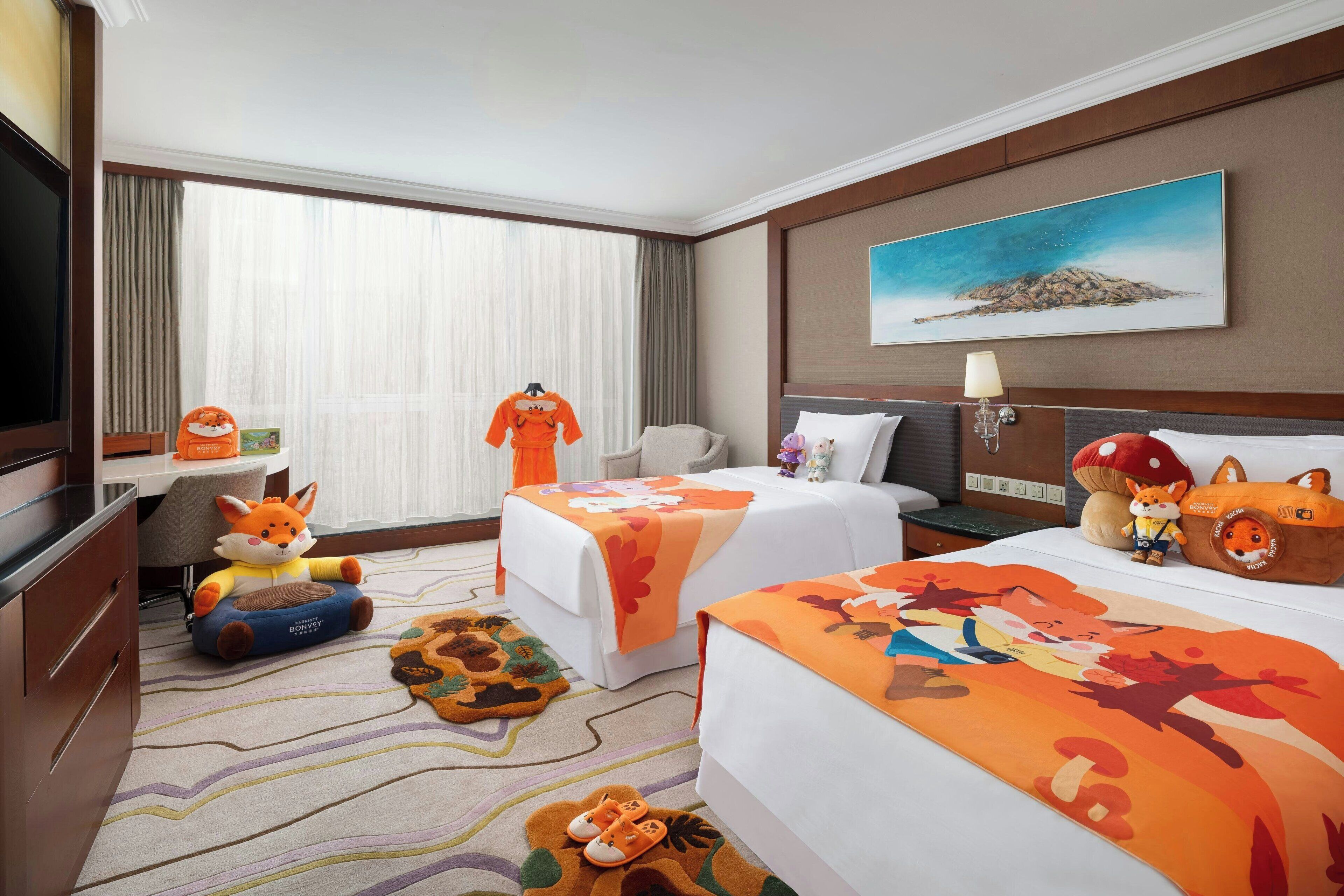 A hotel room with two beds, a TV, a desk with a chair, and a large window with curtains.