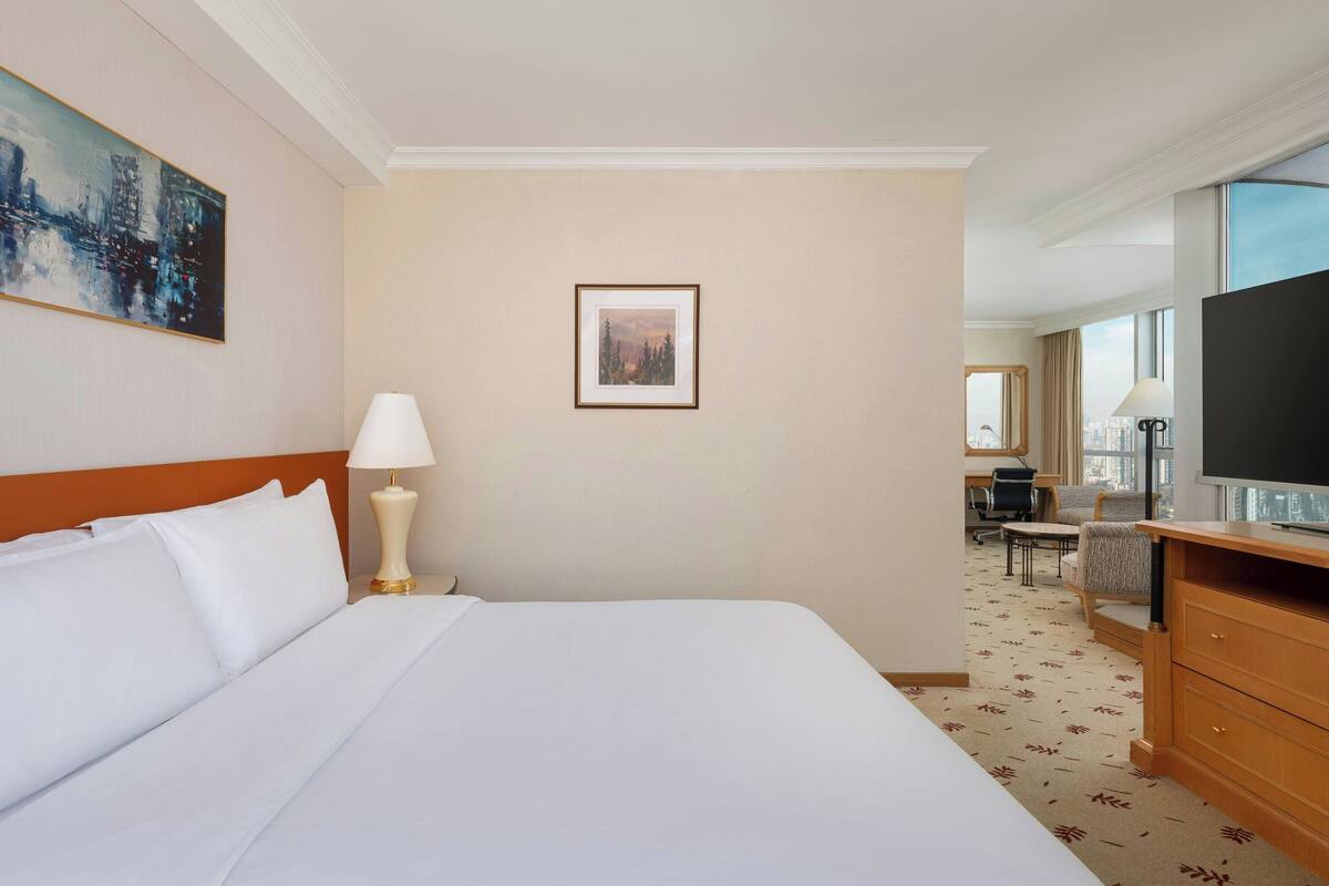 A hotel room with a large bed, a desk with a flat-screen TV, a lamp, and a framed picture on the wall.