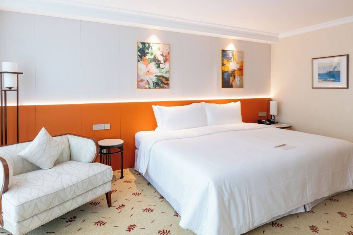 A hotel room with a large bed, a sofa, a small round table, and artwork on the walls.