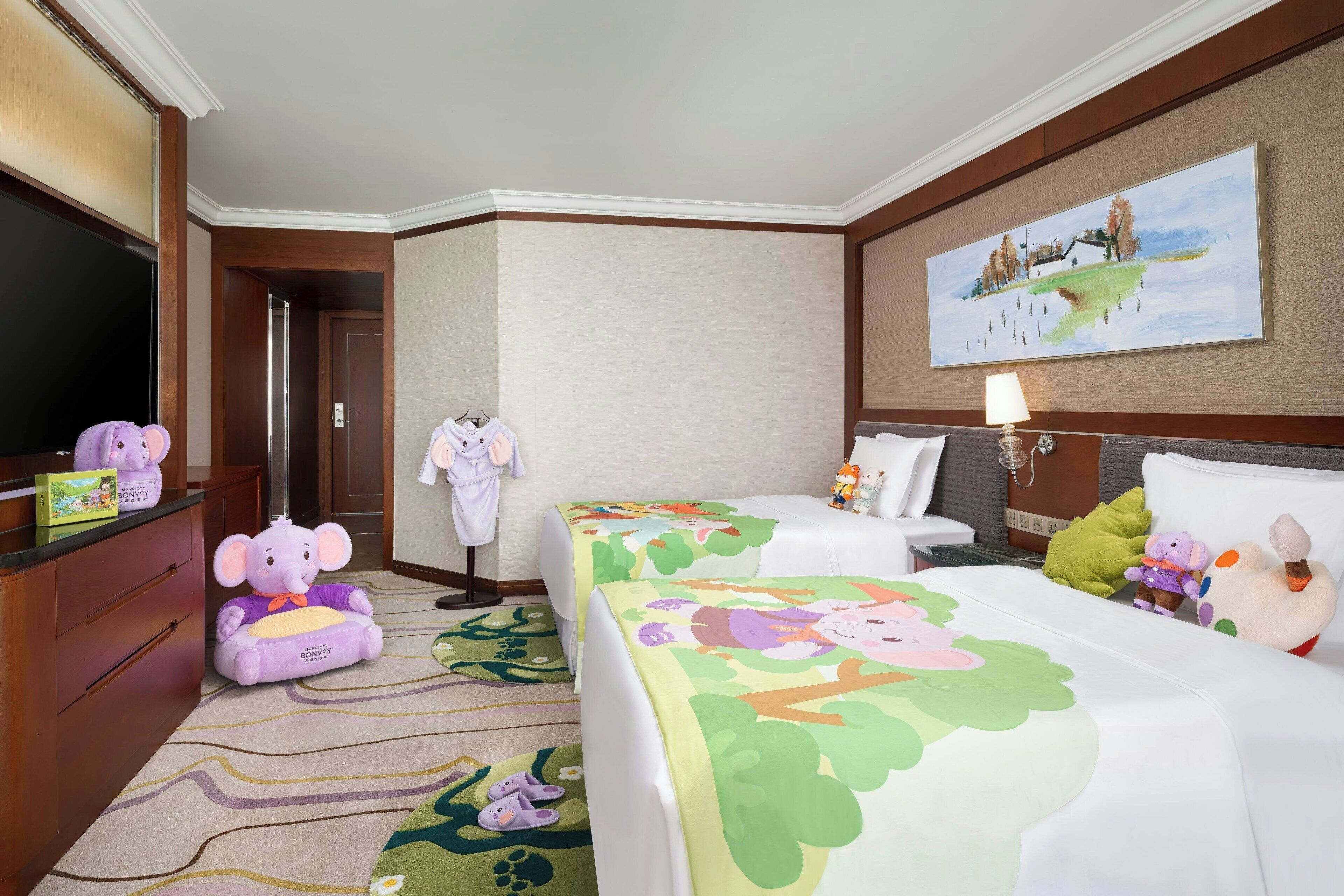 Habitación de hotel con dos camas, televisión, un cuadro y peluches.