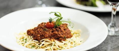 A plate of spaghetti with meat sauce and a cherry tomato garnish.