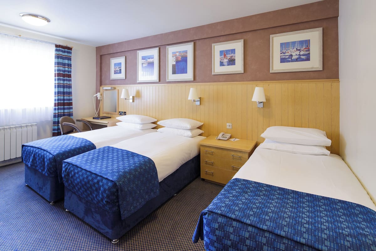 A hotel room with two beds, a desk, a chair, and a window with curtains.