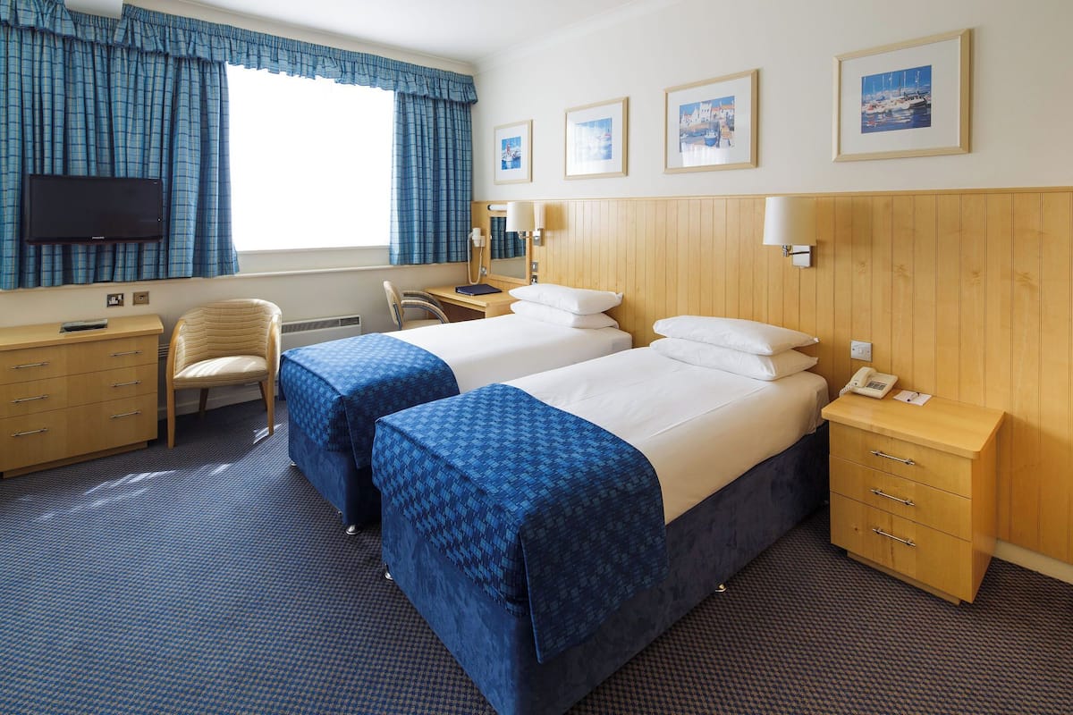 A hotel room with two beds, a desk, a chair, a TV, and framed pictures on the wall.