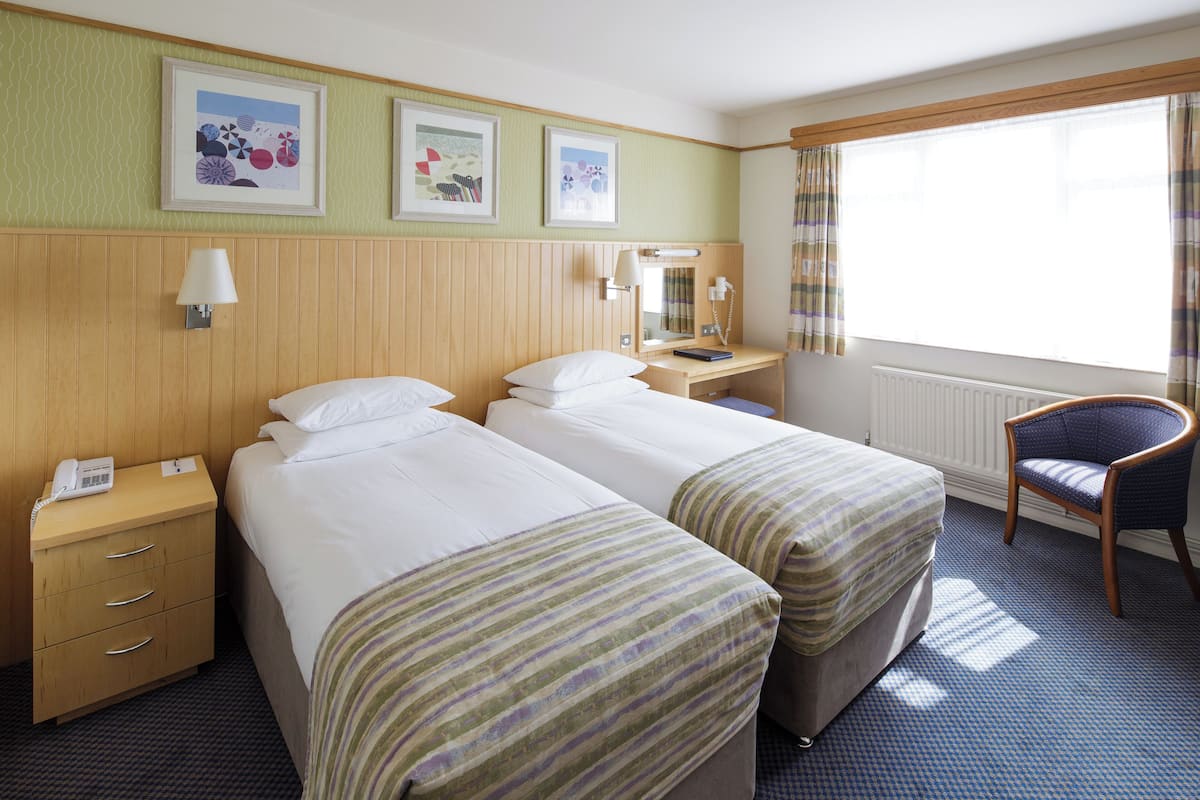 A hotel room with two beds, a desk, a chair, and a window with curtains.