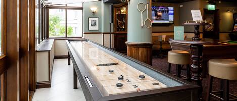 A pool table in a hotel lobby with a bar area and seating.