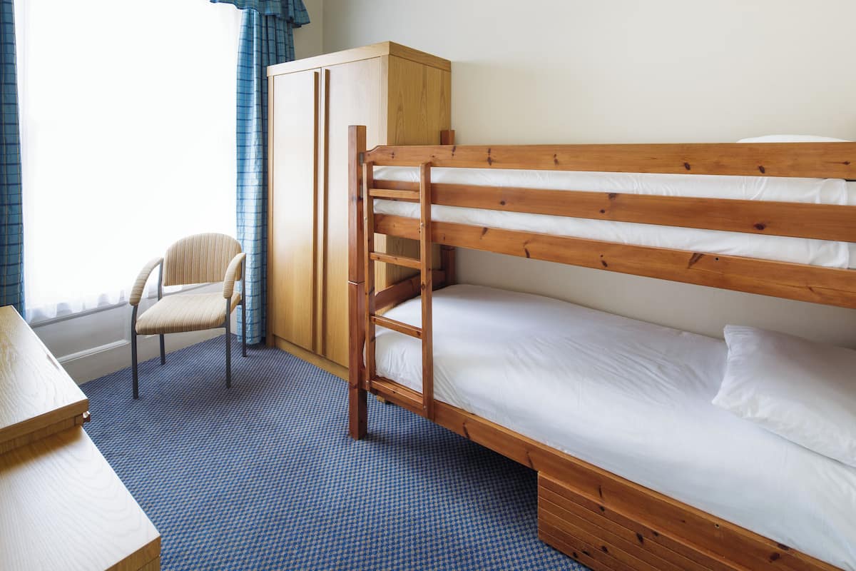 A bunk bed with a wooden frame, a chair, and a wardrobe in a room with a checkered carpet.