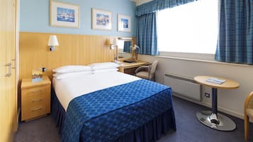 Une chambre d’hôtel avec un grand lit, un bureau avec une chaise, une petite table et une fenêtre avec des rideaux.