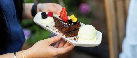 A person holding a white plate with a dessert, including a piece of cake and a scoop of ice cream.