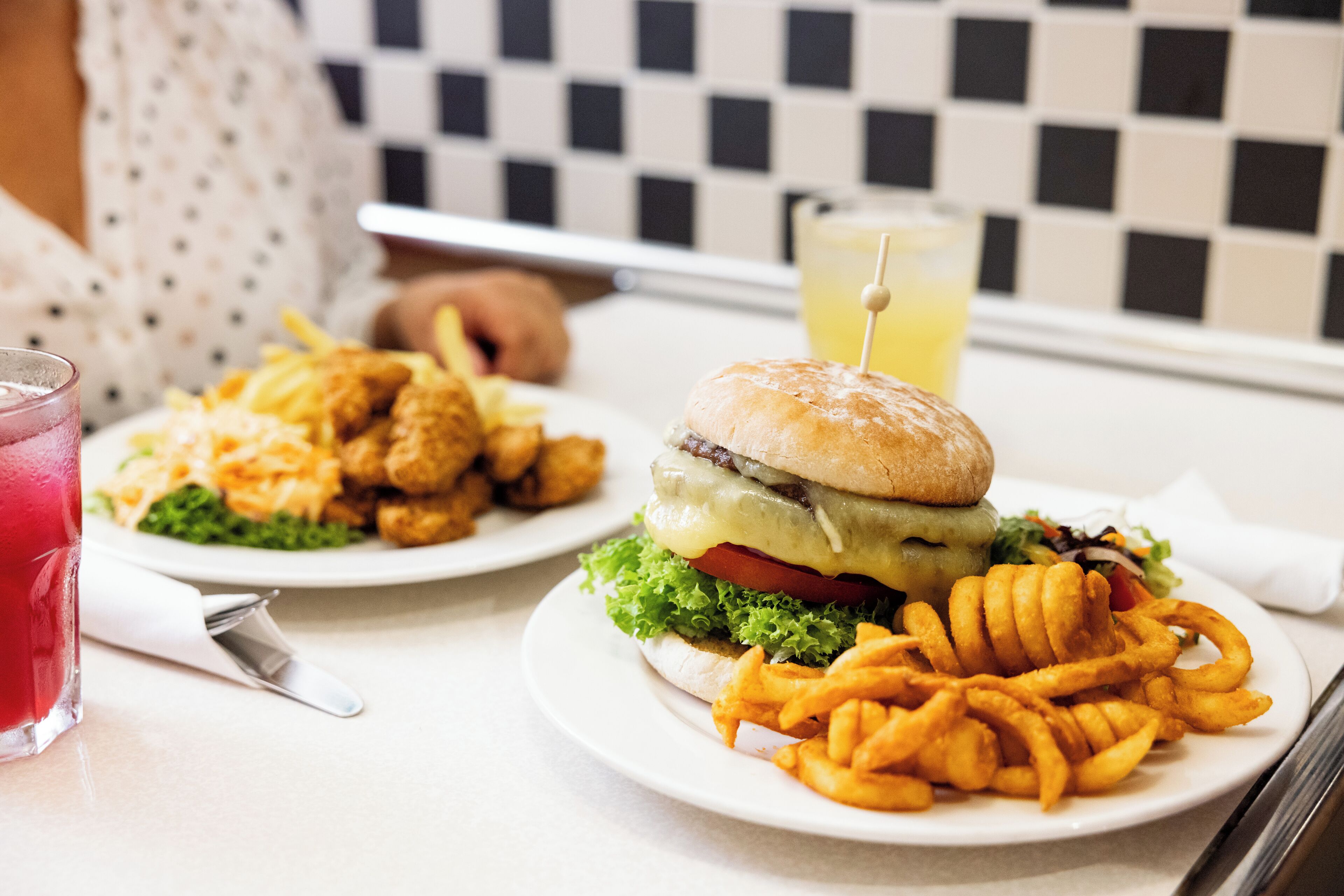 Comida que incluye una hamburguesa, papas fritas y una bebida sobre una mesa.