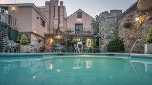 Una piscina con un muro de piedra y un edificio con balcón.