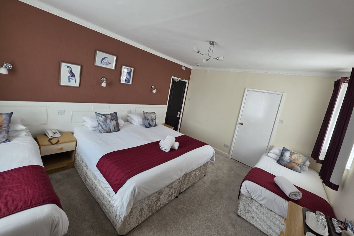 A hotel room with two beds, a desk, a telephone, and a door.