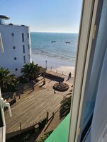 A view of a beachside promenade with a wooden deck, palm trees, and a building with multiple windows.
