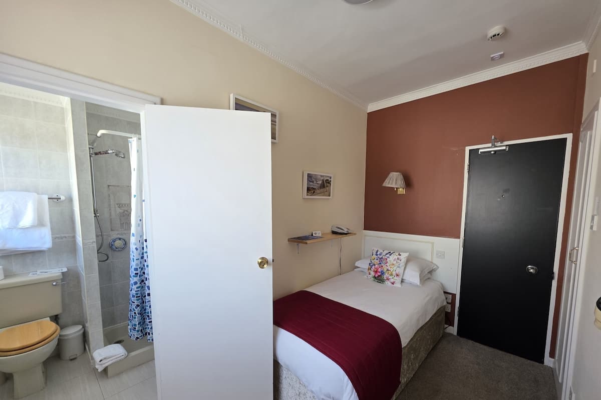 A hotel room with a bed, a shower, a toilet, and a door.