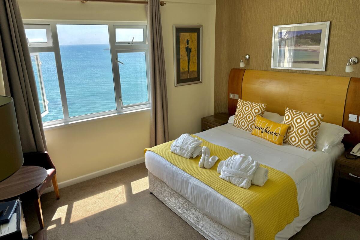 A hotel room with a large bed, a view of the sea, and a framed picture on the wall.