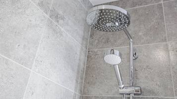 Une douche équipée d’un pommeau de douche à main et d’un pommeau de douche fixe au plafond, dans une salle de bain carrelée.