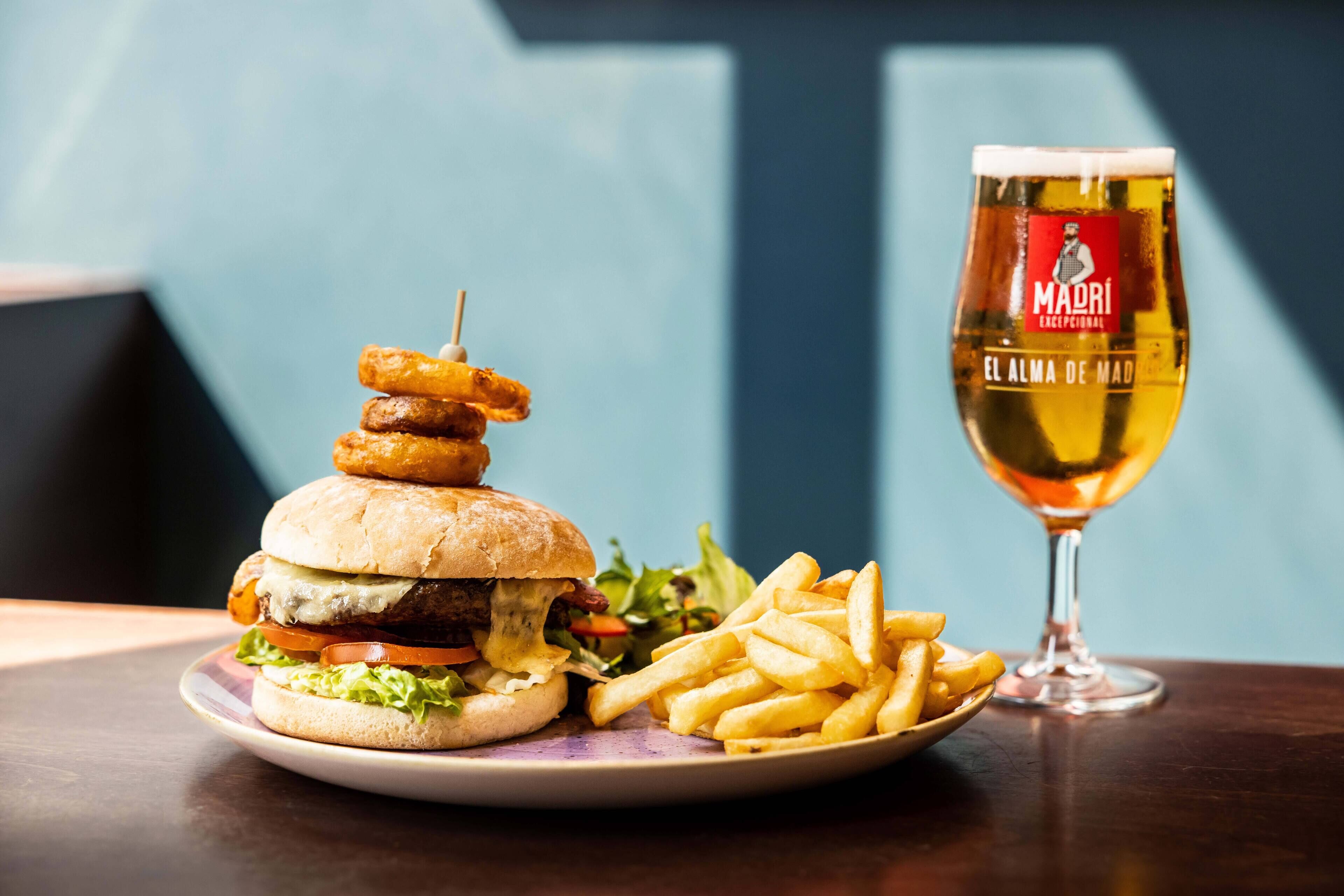 Una hamburguesa con papas fritas y una cerveza en una mesa.