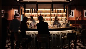 A bar area with a counter, stools, and a shelf with bottles. - Pomme d'Or Hotel (St. Helier)