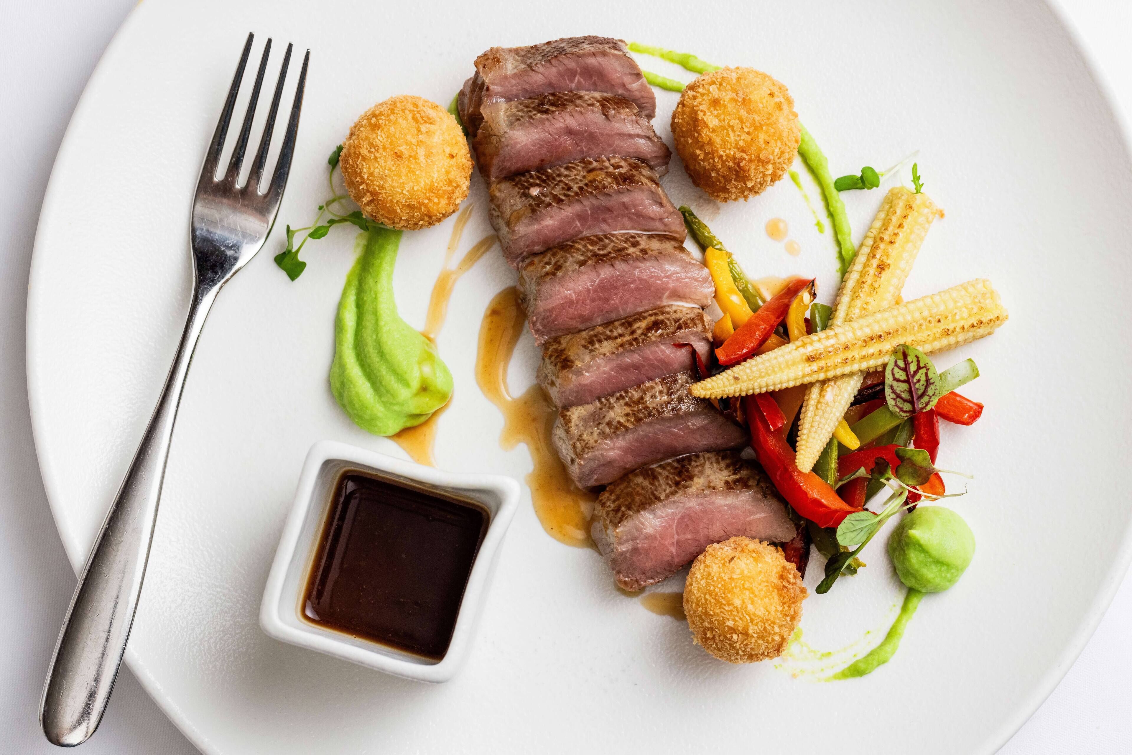 A plate with sliced meat, corn, and a small bowl of sauce.