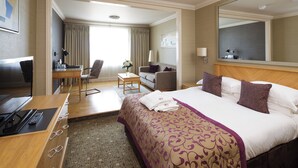 A hotel room with a large bed, a desk with a computer, a chair, and a small table with a vase of flowers. - Pomme d'Or Hotel (St. Helier)