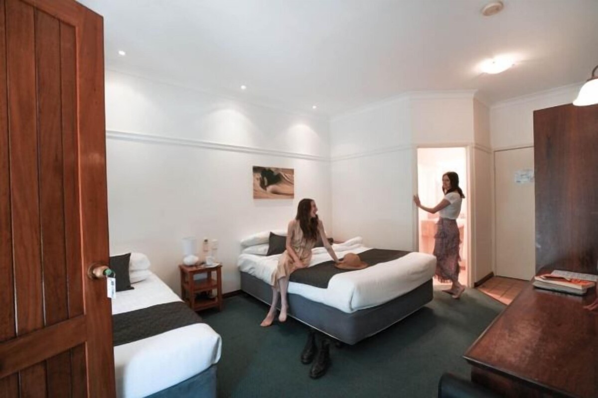 Habitación de hotel con dos camas, un armario de madera, una mesita y un cuadro en la pared.