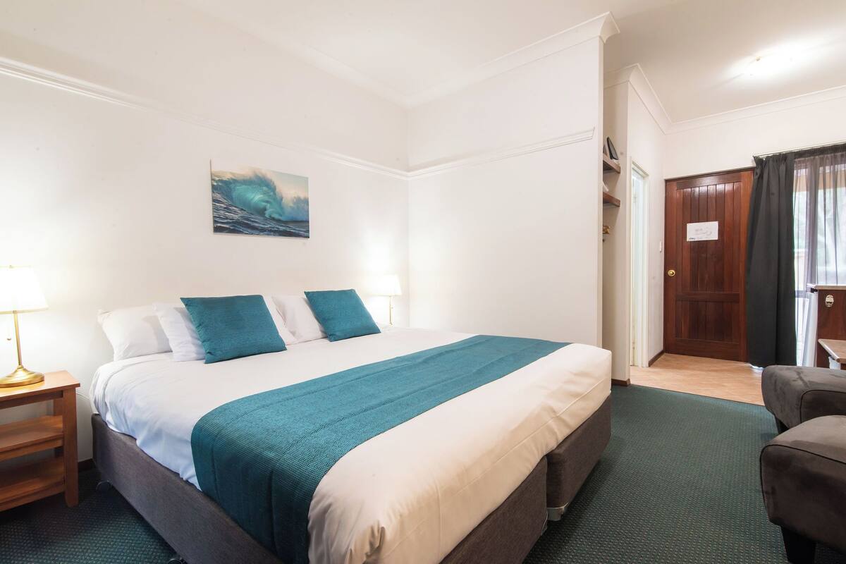 Une chambre d’hôtel avec un grand lit, une table de chevet, une chaise et une porte avec une pancarte.