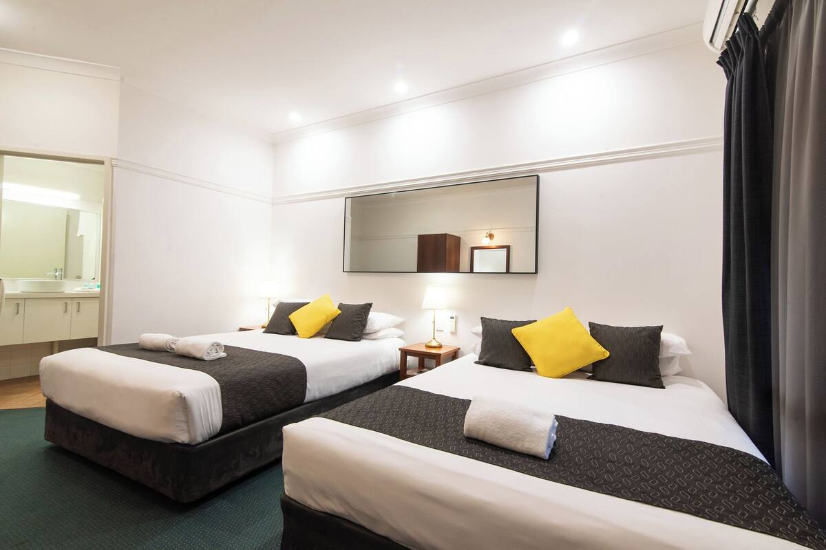 Une chambre d’hôtel avec deux lits, un miroir, une table de chevet et une salle de bain visible au fond.