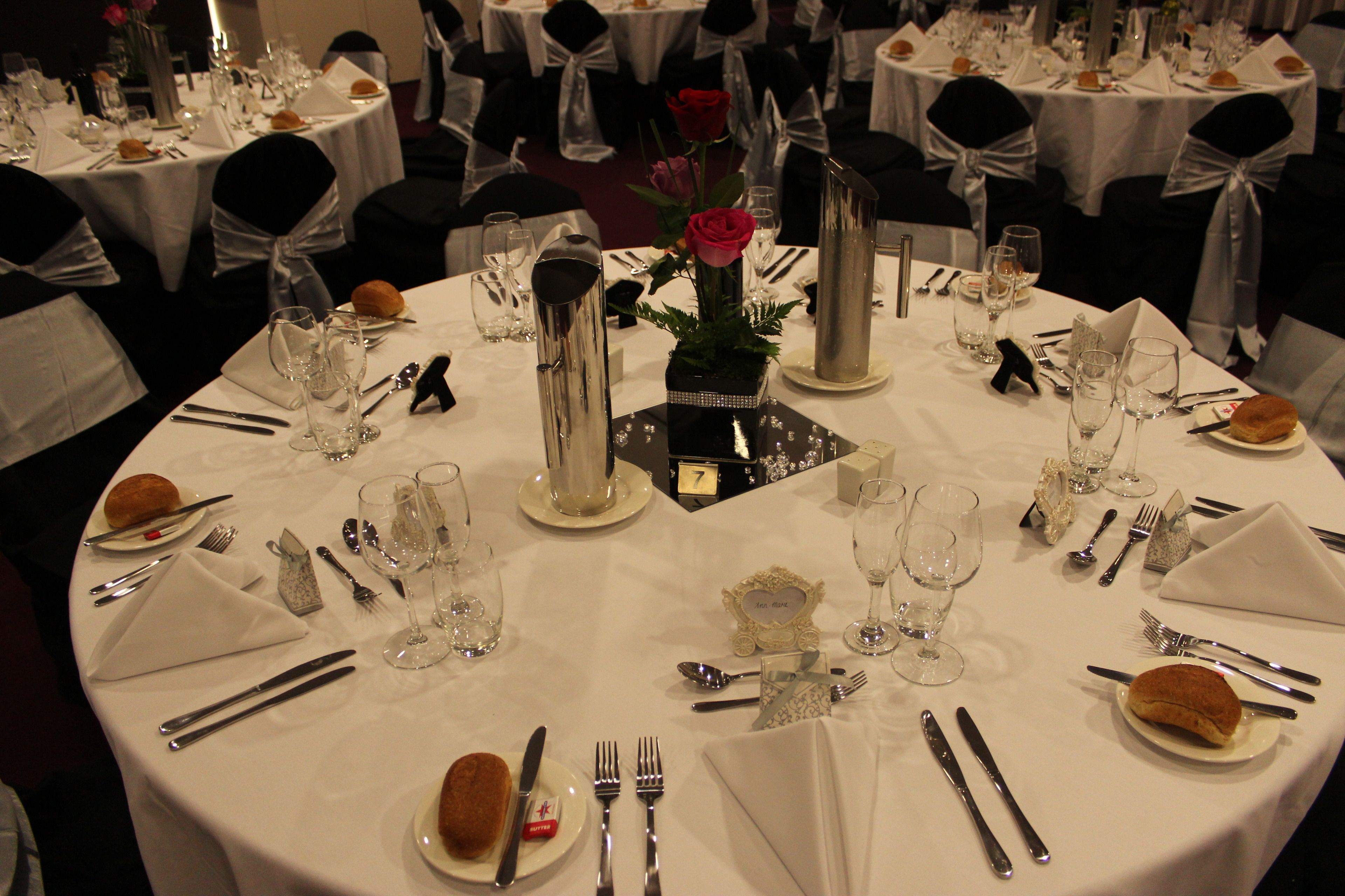 A formal dining setup with round tables, white tablecloths, and black chair sashes.