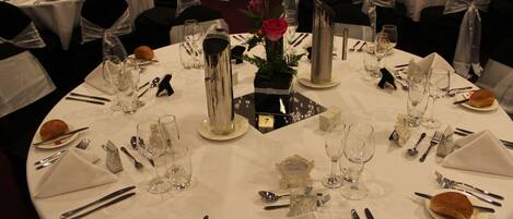 A formal dining setup with round tables, white tablecloths, and black chair sashes.