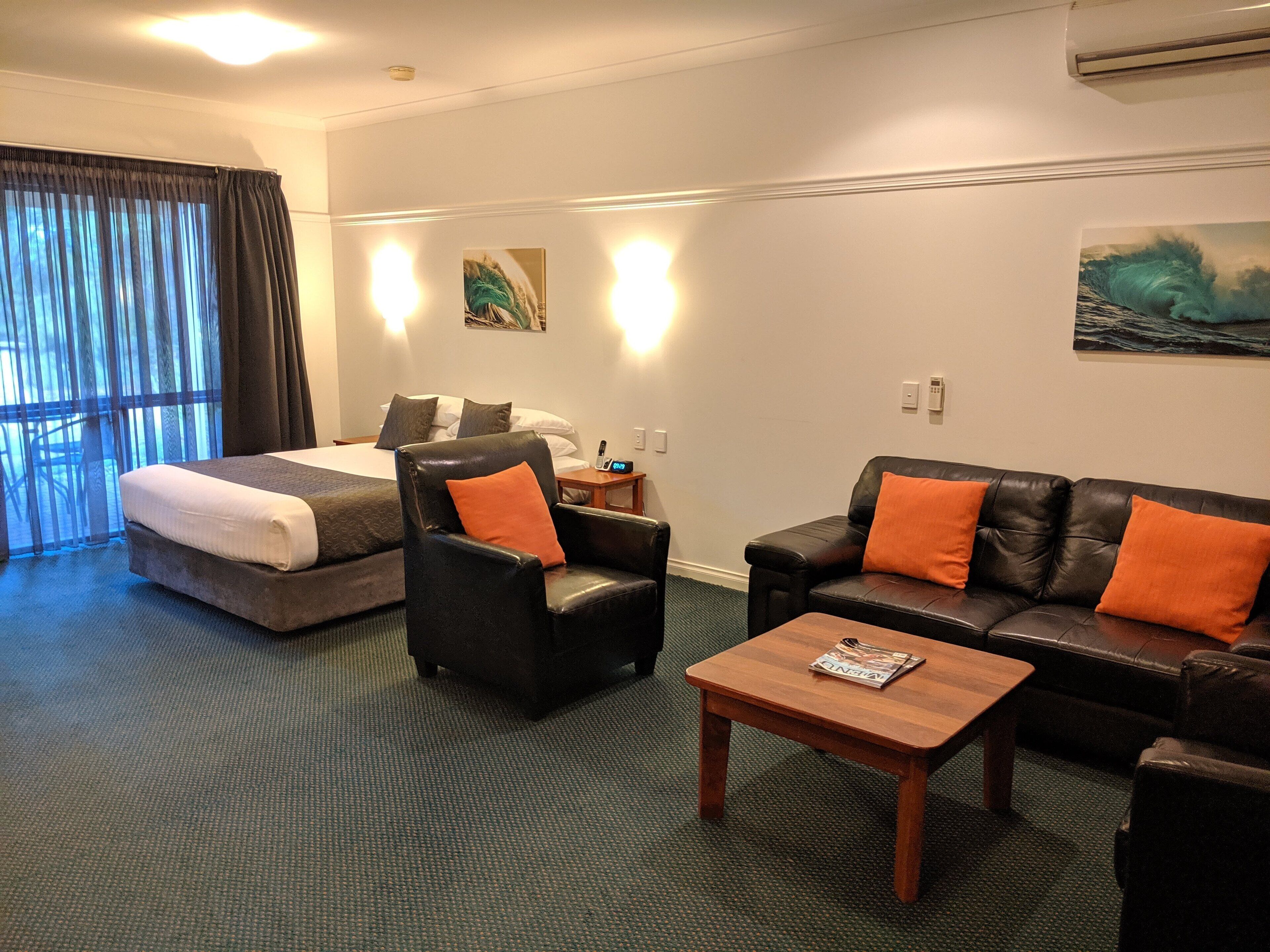 Ein Hotelzimmer mit einem Bett, einem Ledersessel, einer Ledersofa und einem Holztisch sowie einem Gemälde an der Wand.
