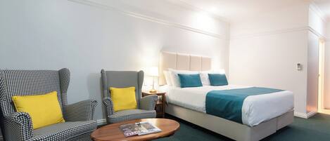 A hotel room with a bed, two armchairs, a small table, and a nightstand with a lamp.