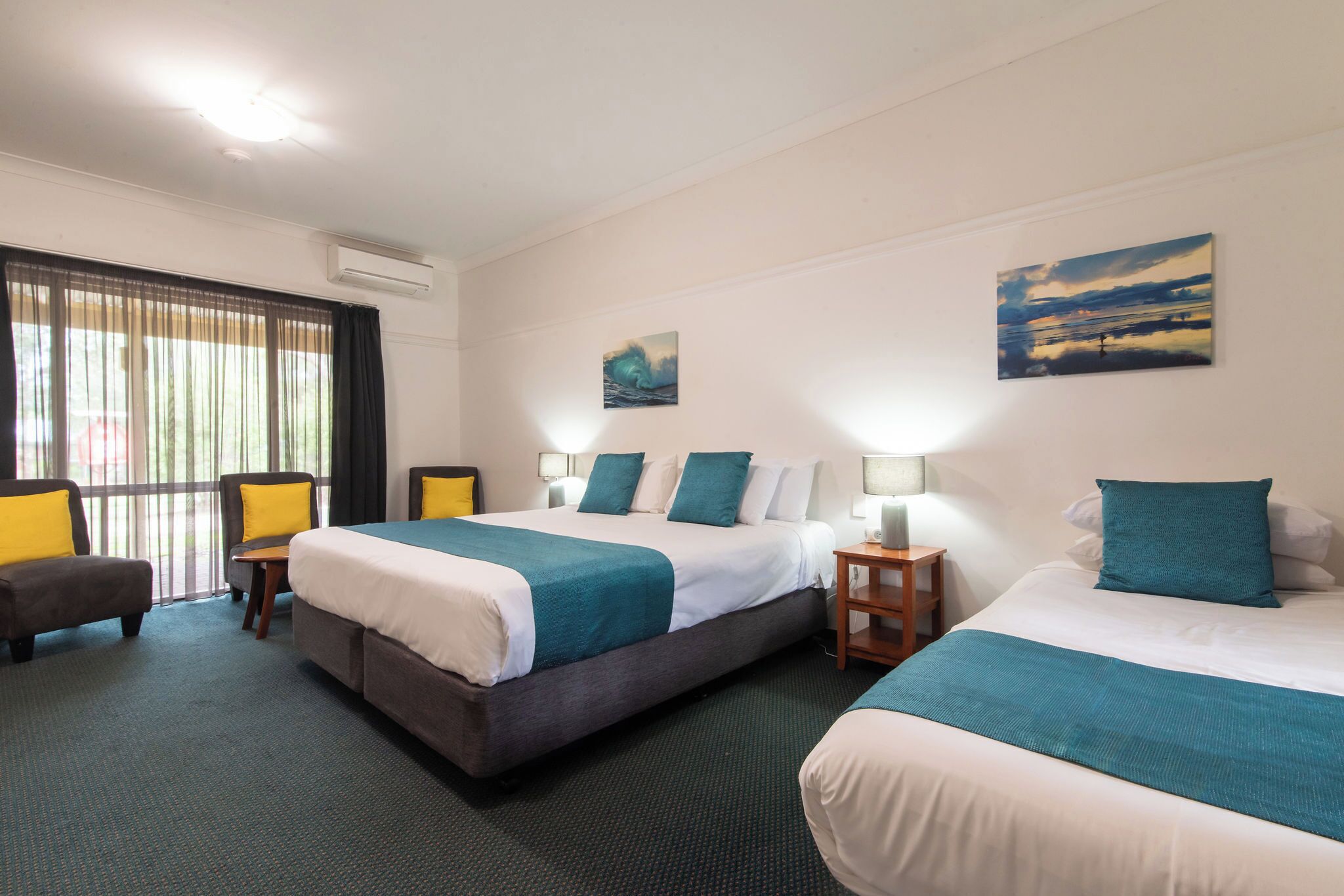A hotel room with two beds, a desk, a chair, and artwork on the walls.