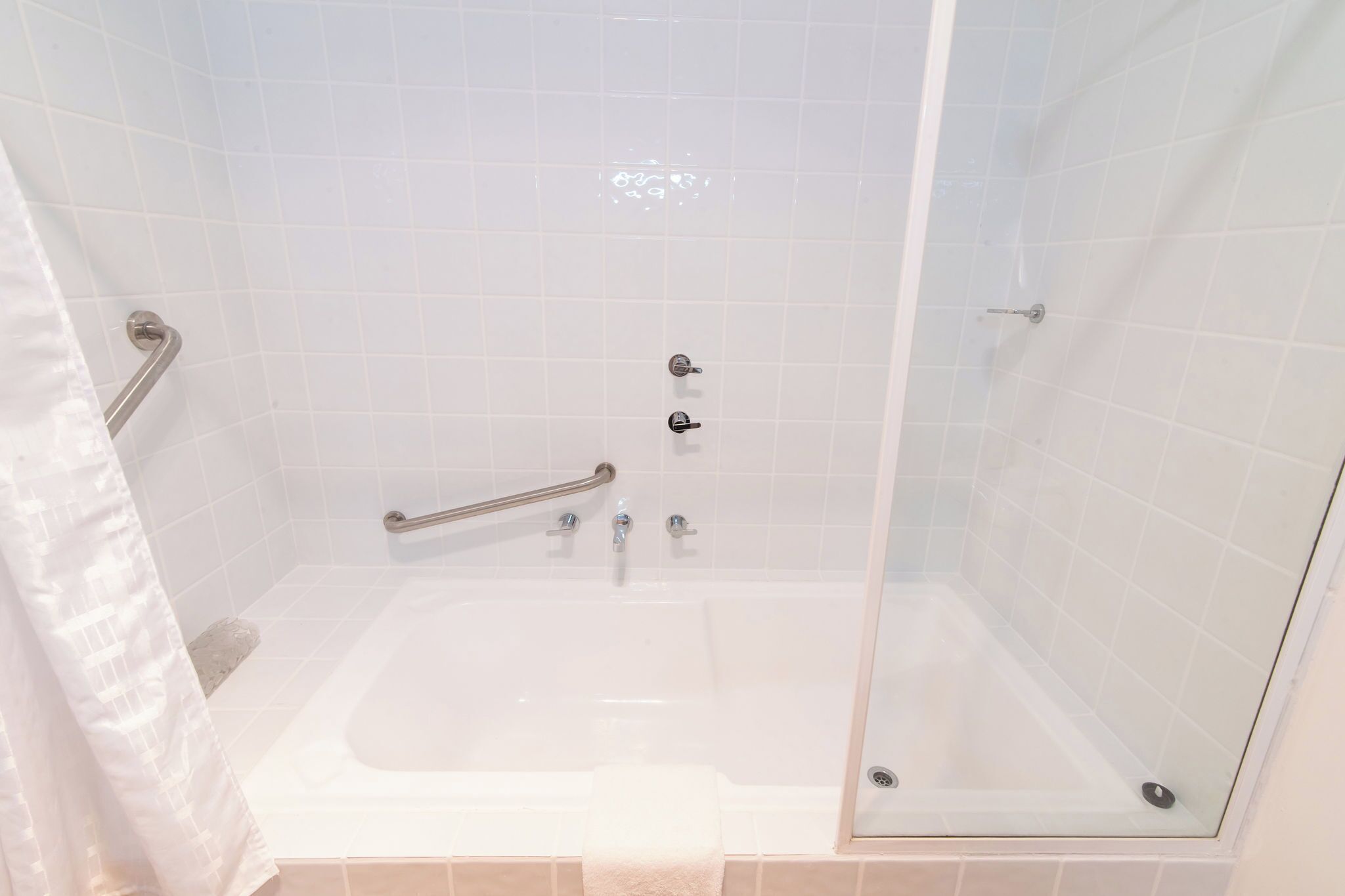 A modern bathroom with a glass-enclosed shower, a bathtub, and a handrail.