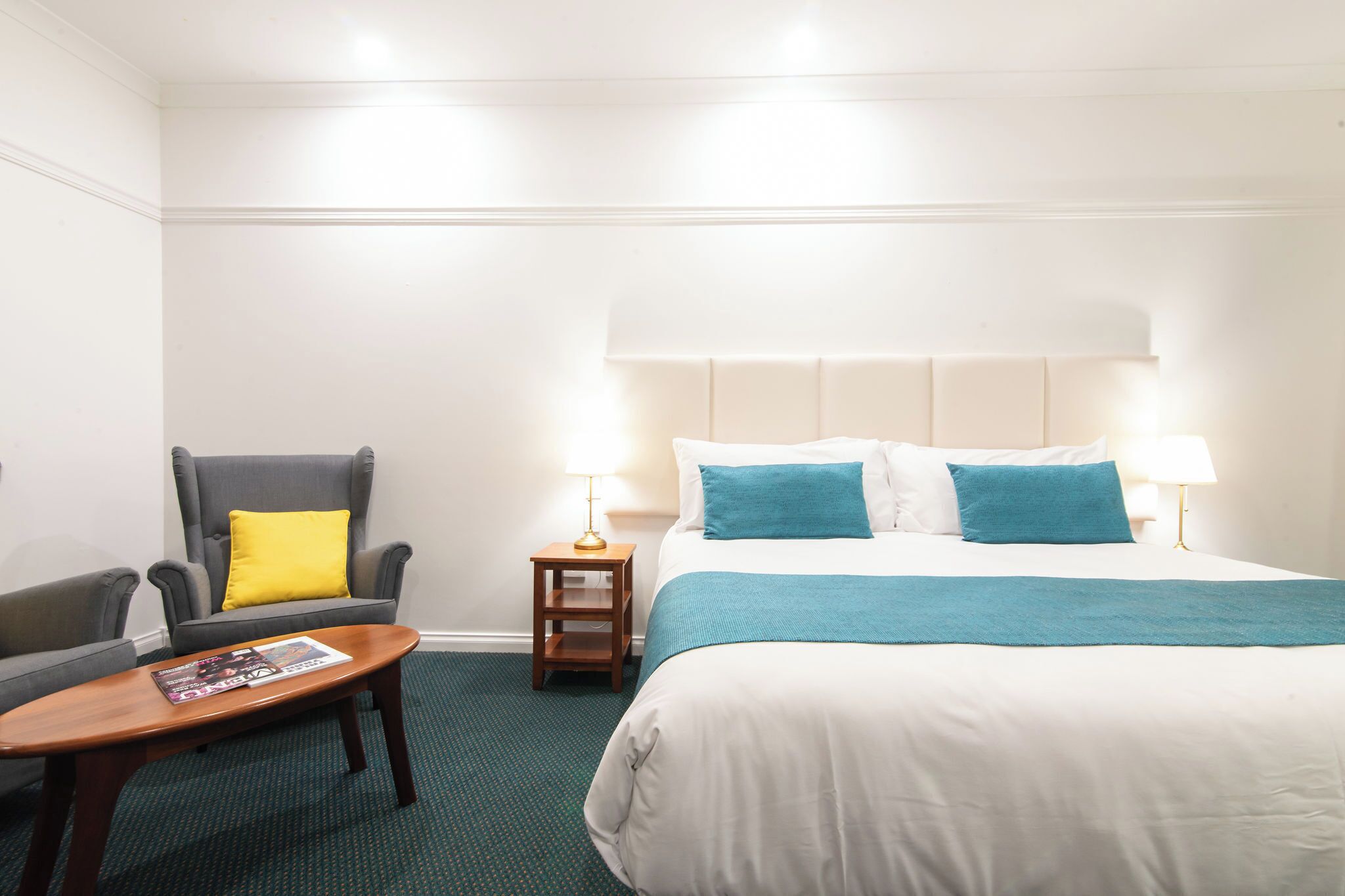 A hotel room with a bed, a chair, a small table, and two bedside lamps.