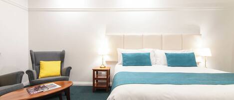 A hotel room with a bed, a chair, a small table, and two bedside lamps.