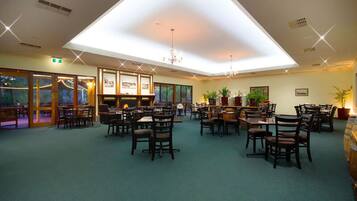 A spacious dining area with multiple tables and chairs, a high ceiling with skylights, and potted plants.