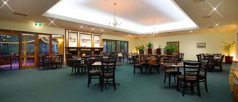A spacious dining area with multiple tables and chairs, a high ceiling with skylights, and potted plants.