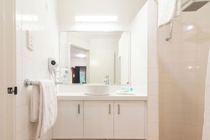 Un baño moderno con un lavamanos, espejo y ducha blancos.